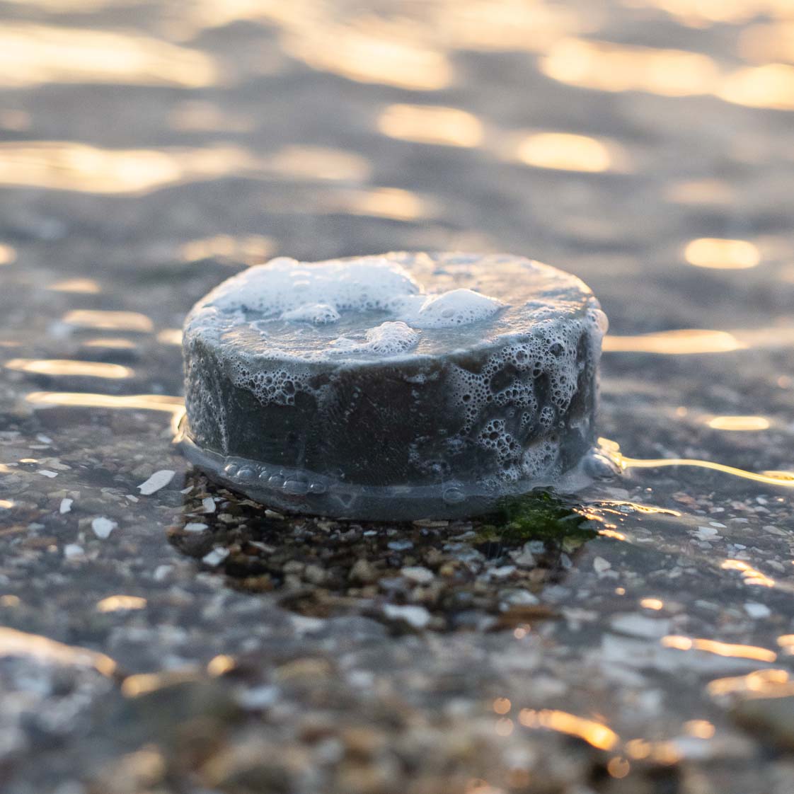 OGO Soap's Ocean Clay Cleansing Bar covered in lather, slightly immersed in the ocean.